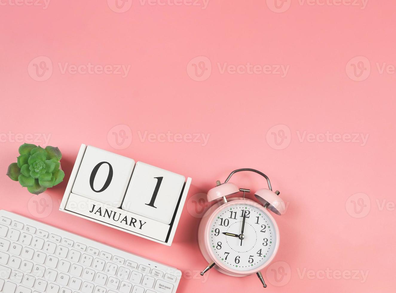 flat lay of computer keyboard, wooden calendar 01 January, pink vintage alarm clock 9 o'clock and succulent plant pot on pink background. First morning of new year. photo