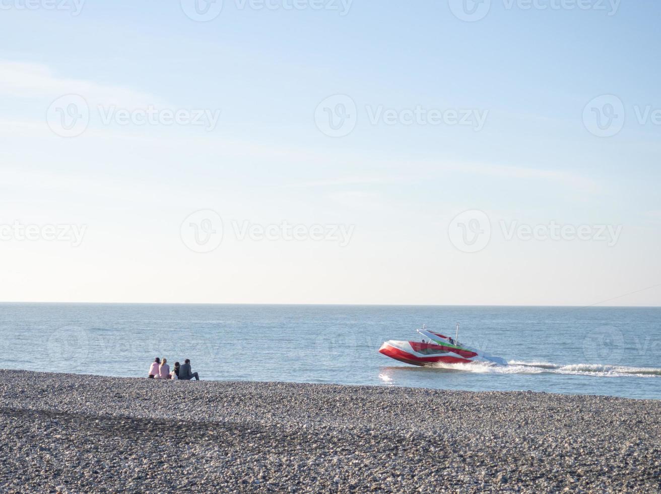 People on the spring pebble beach. Vacation on the beach. Relaxation at sea. Rocky seashore. Pebble beach. Boats on the water. photo