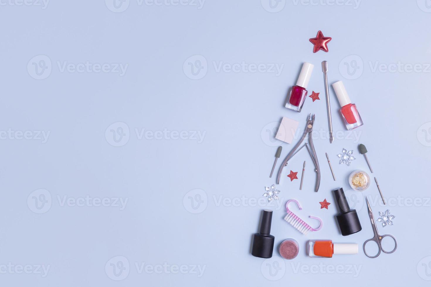 Manicure tools and nail polishes are laid out in the shape of a Christmas tree with copy space on blue background with copy space photo