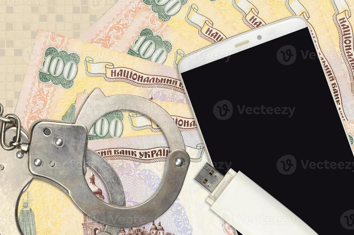 100 Ukrainian hryvnias bills and smartphone with police handcuffs. Concept of hackers phishing attacks, illegal scam or malware soft distribution photo