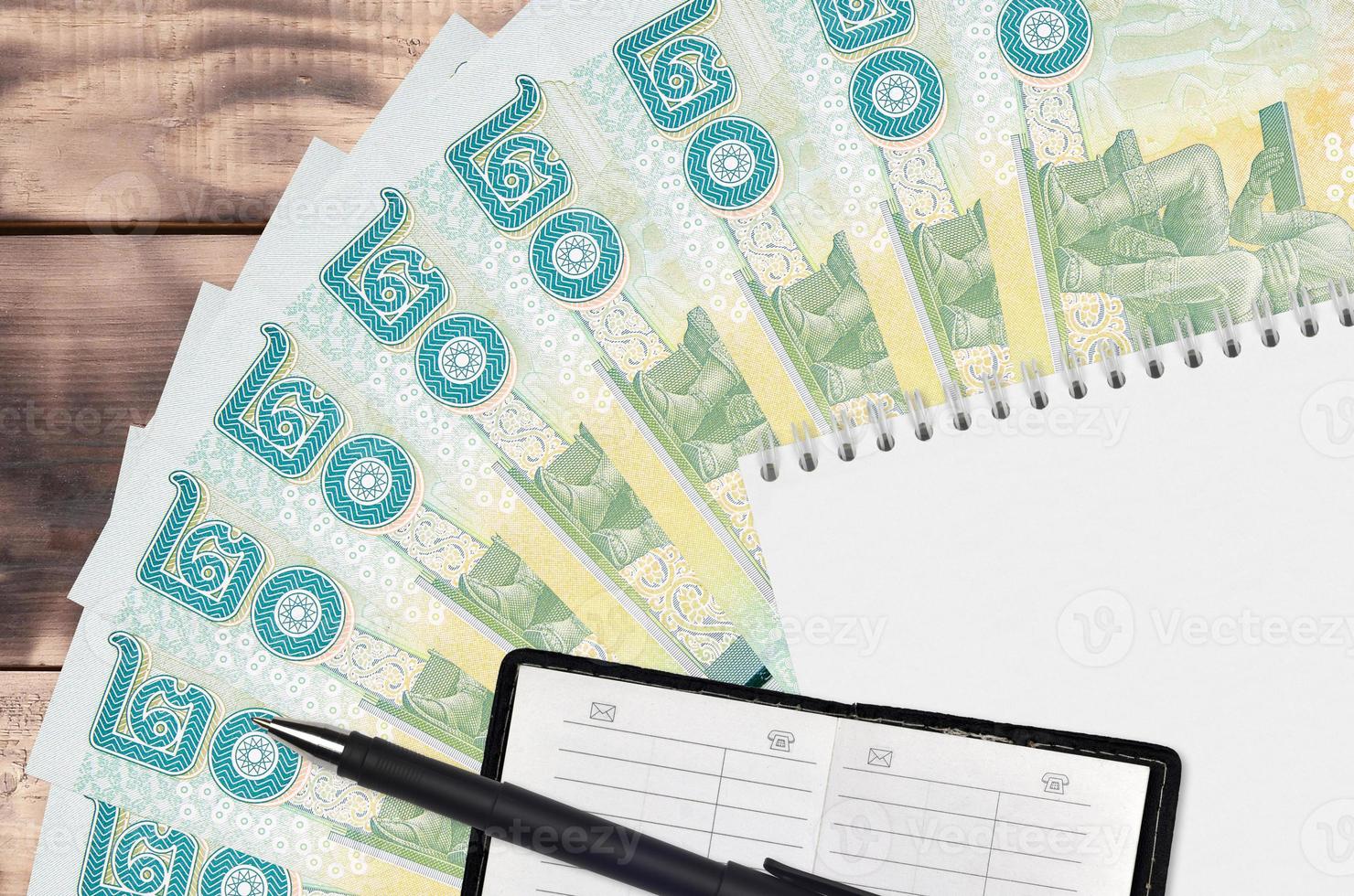 Abanico de billetes de 20 baht tailandeses y bloc de notas con libreta de contactos y bolígrafo negro. concepto de planificación financiera y estrategia empresarial foto
