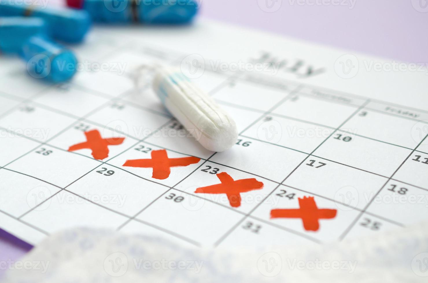 almohadillas menstruales y tampones en el calendario del período de menstruación con marcas de cruz roja sobre fondo lila foto
