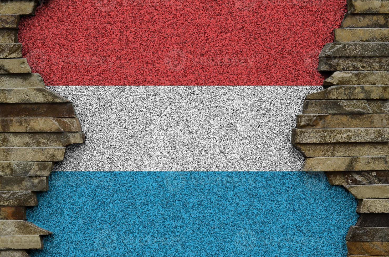 Luxembourg flag depicted in paint colors on old stone wall closeup. Textured banner on rock wall background photo