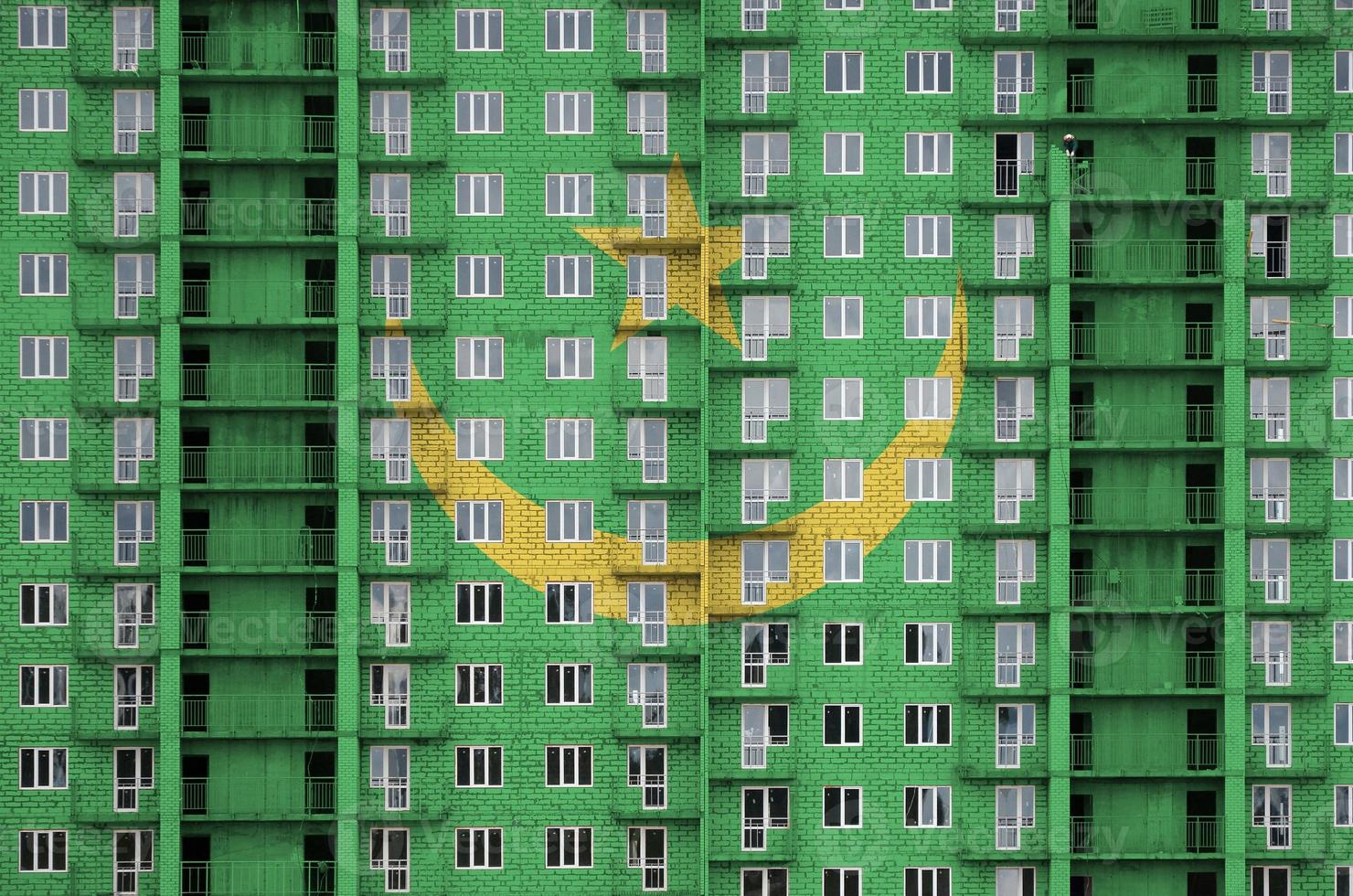 Mauritania flag depicted in paint colors on multi-storey residental building under construction. Textured banner on brick wall background photo