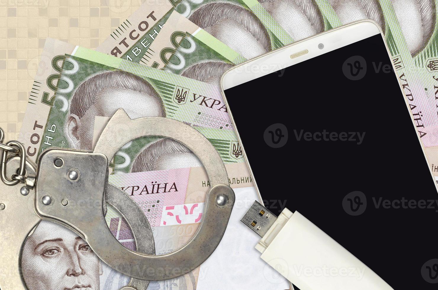 500 Ukrainian hryvnias bills and smartphone with police handcuffs. Concept of hackers phishing attacks, illegal scam or malware soft distribution photo