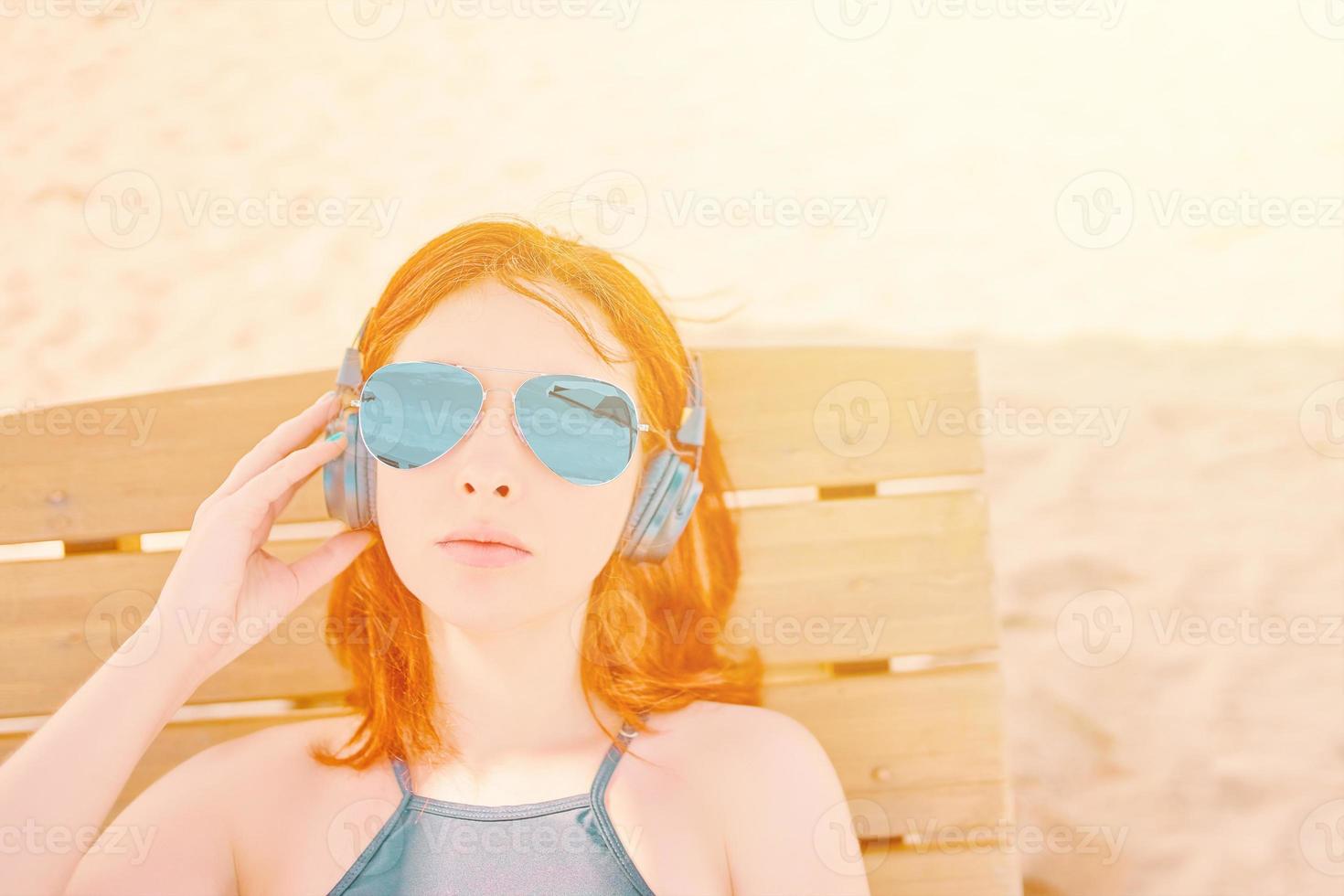 Beautiful woman in sunglasses listening to music on the beach. photo