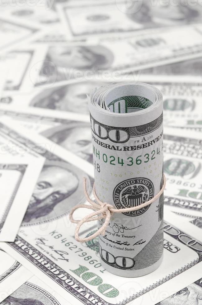 US dollars rolled up and tightened with band lies on a lot of american banknotes with blurred background photo