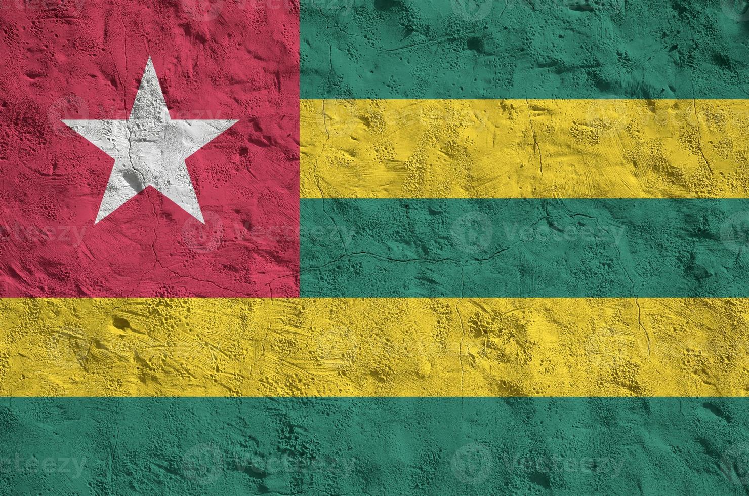 Togo flag depicted in bright paint colors on old relief plastering wall. Textured banner on rough background photo