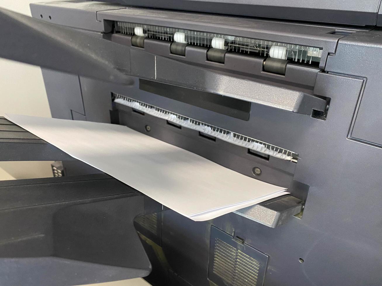 A white sheet of paper comes out of an office printer for printing photo
