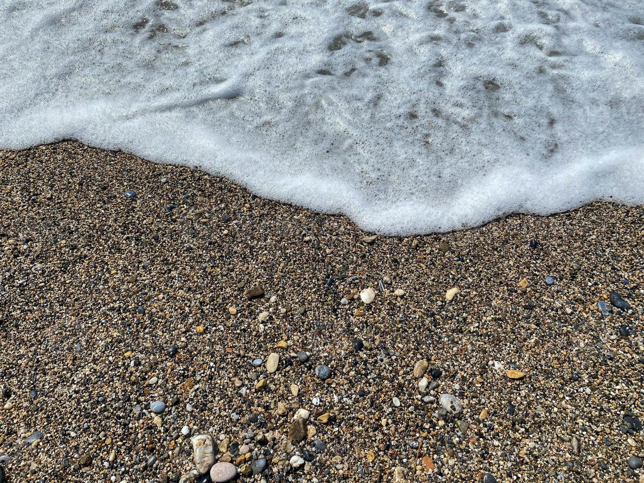 olas de agua en el mar y arena con pequeñas piedras multicolores naturales en la orilla del mar, pequeños guijarros en la playa. fondo, textura foto