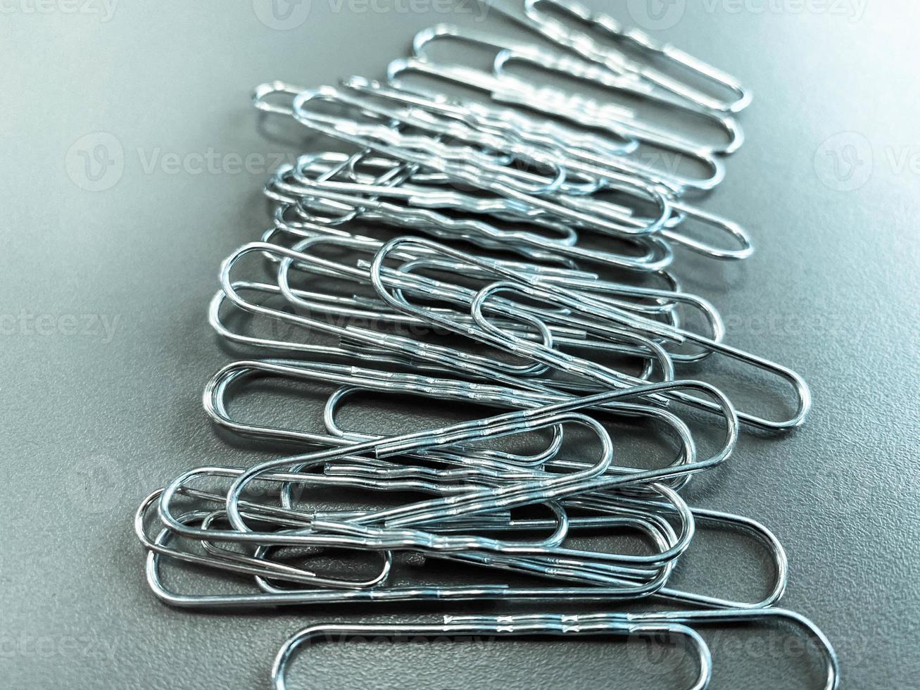 Shiny metal paper clips on a desktop with stationery in a business office. Close view photo