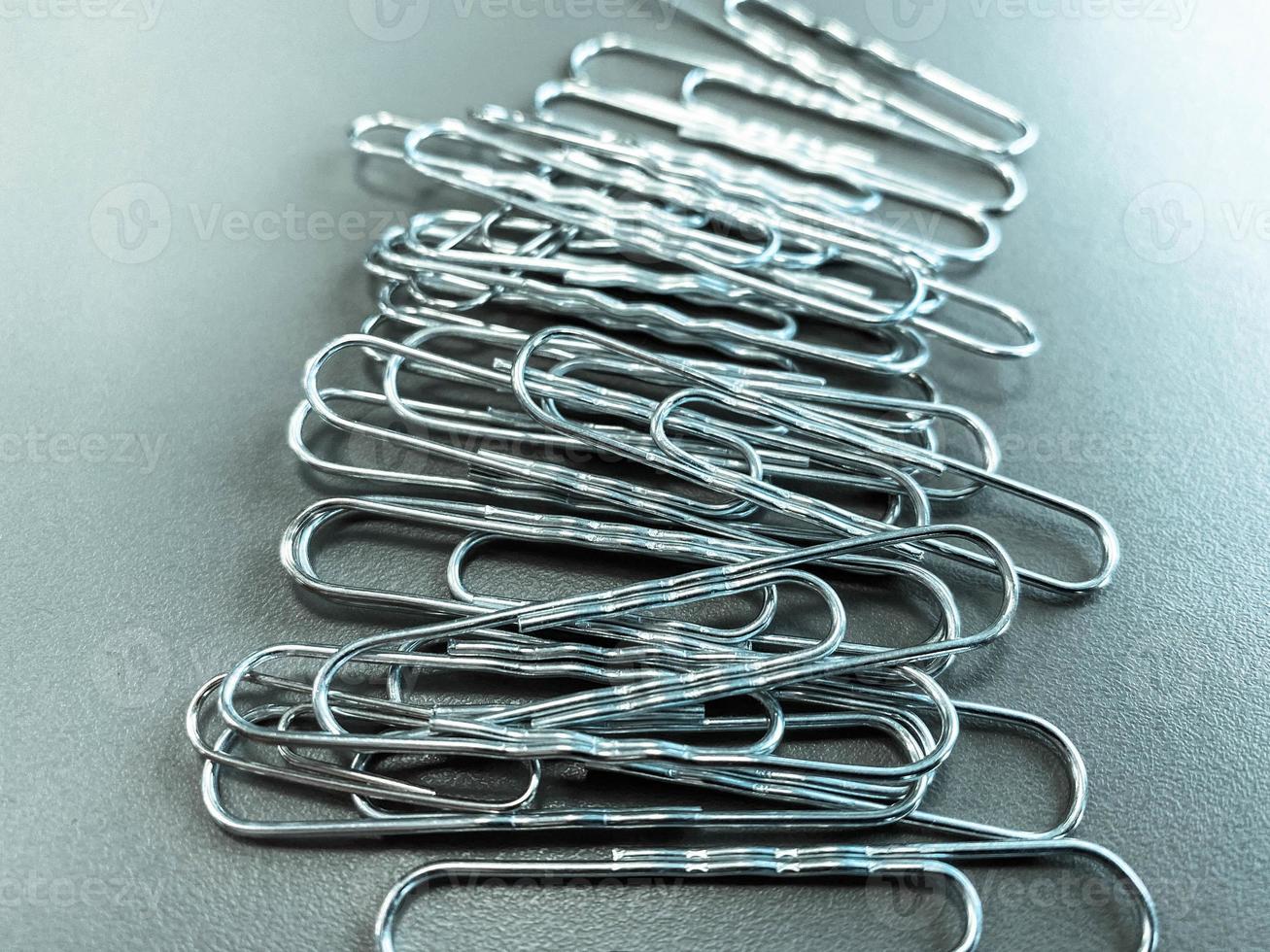 Shiny metal paper clips on a desktop with stationery in a business office. Close view photo