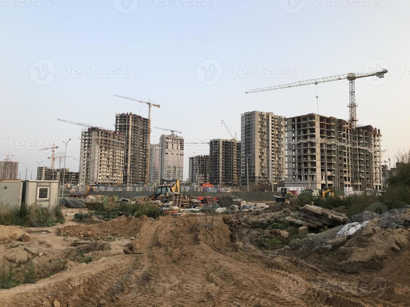 tall houses in the city center. houses are being built with a crane, the crane is carrying heavy concrete blocks. there are many glass panoramic windows in the houses photo