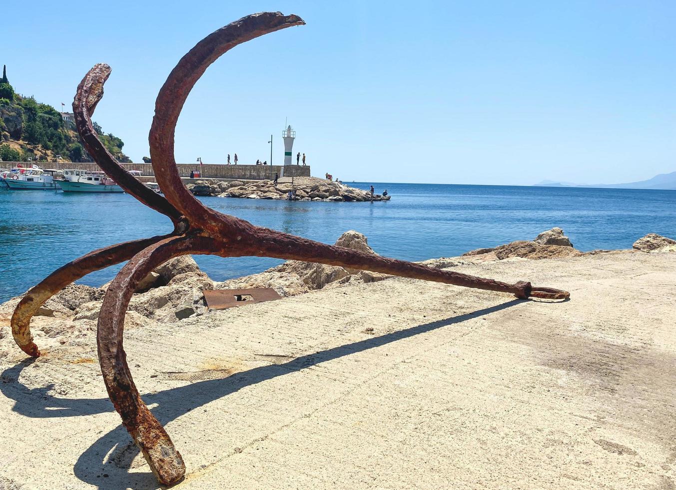 old, rusty anchor on the seashore. at the port with ships and yachts there is an anchor. tourists can see rust at anchor. the anchor lies on the asphalt, left after a boat trip photo