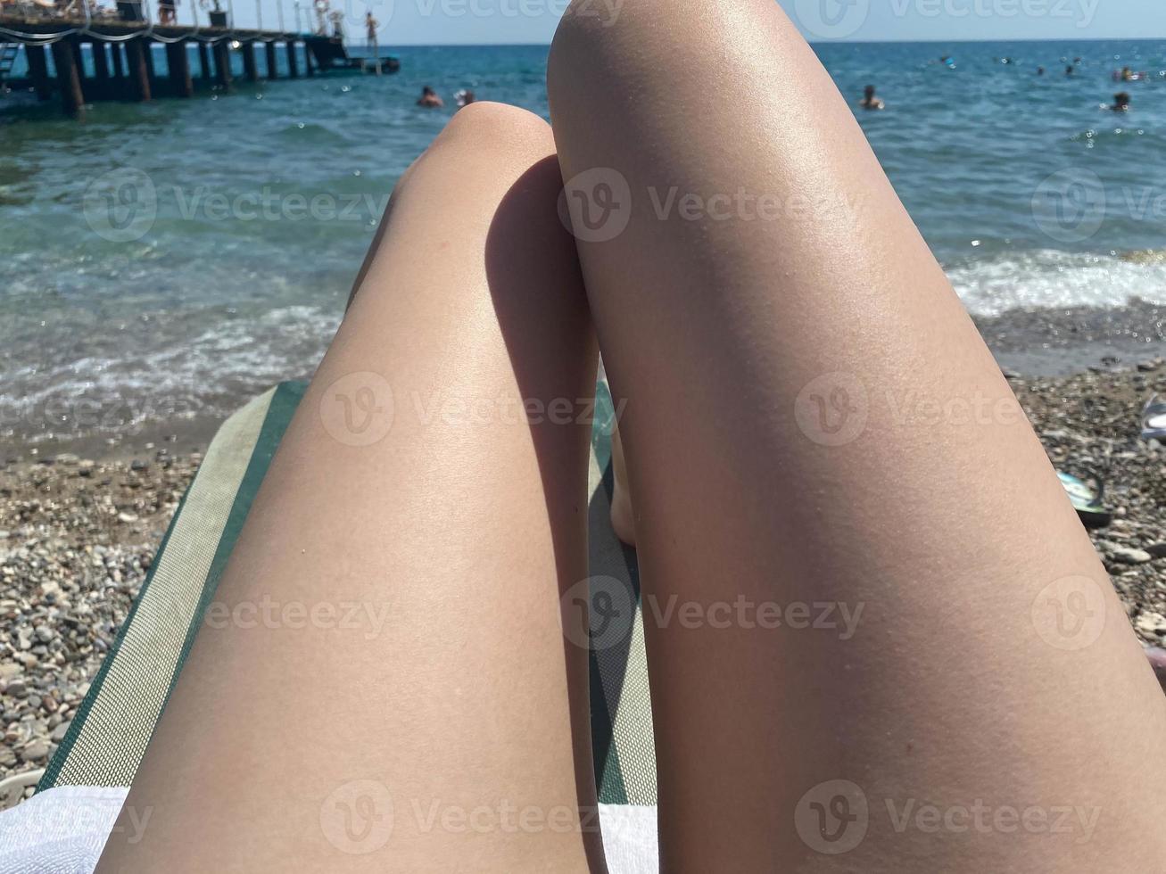 Beautiful legs of a woman with a pedicure having a rest on a sun lounger on the beach by the sea photo