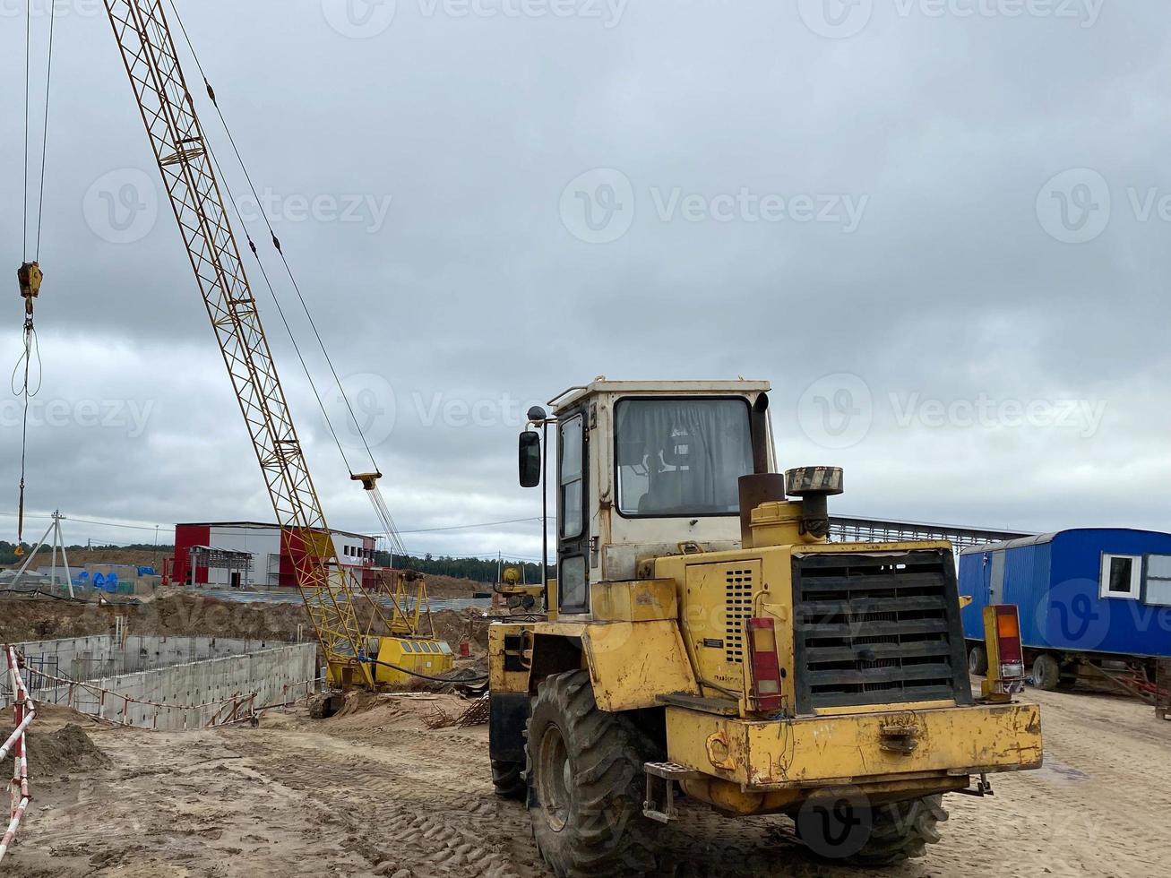 Multiple cars, excavators, trucks, loaders, concrete mixers and construction machinery in large parking lot in industrial territory, next to concrete and asphalt factory photo