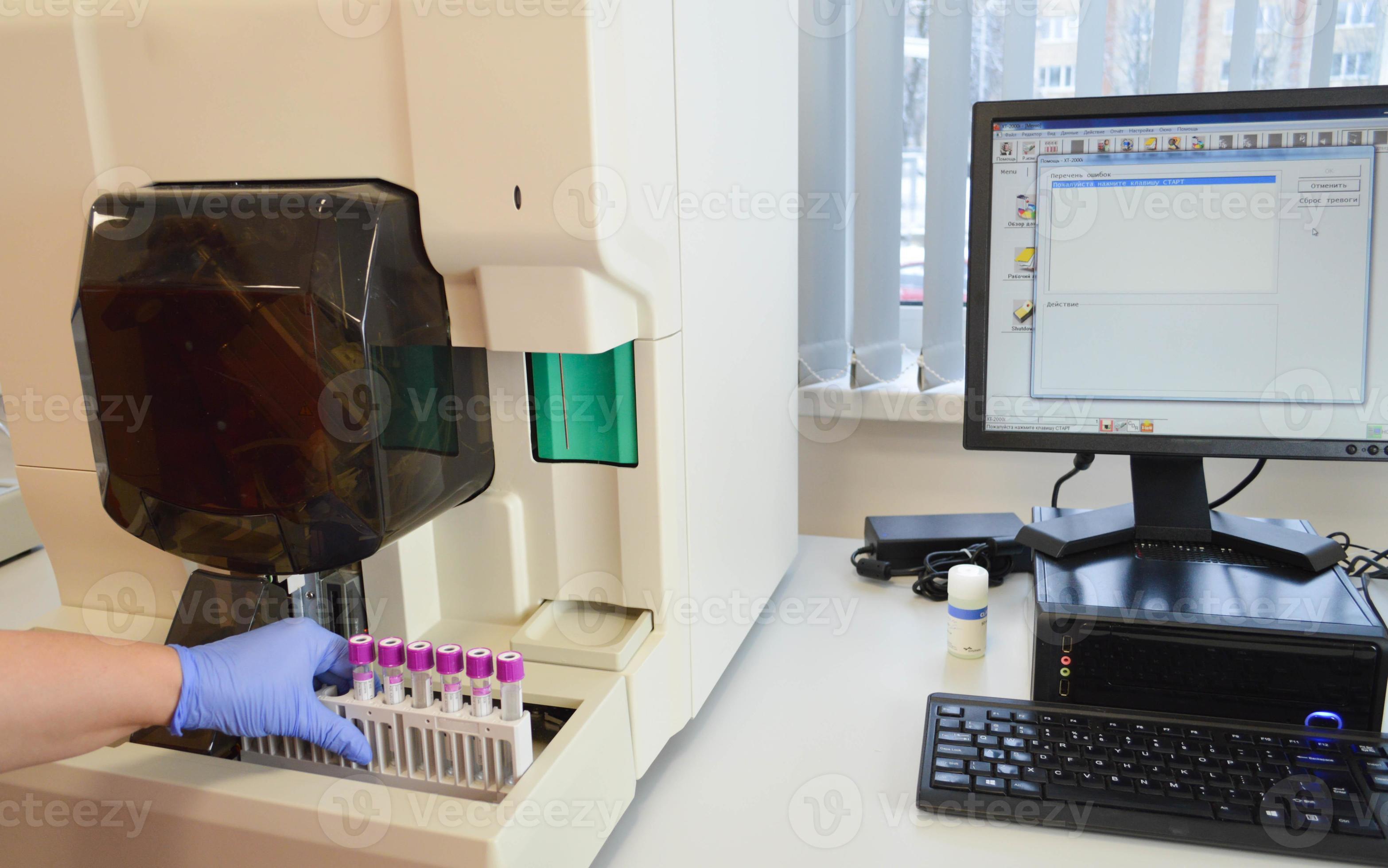 the doctor puts test tubes into the analyzer to perform research. analysis data is displayed on