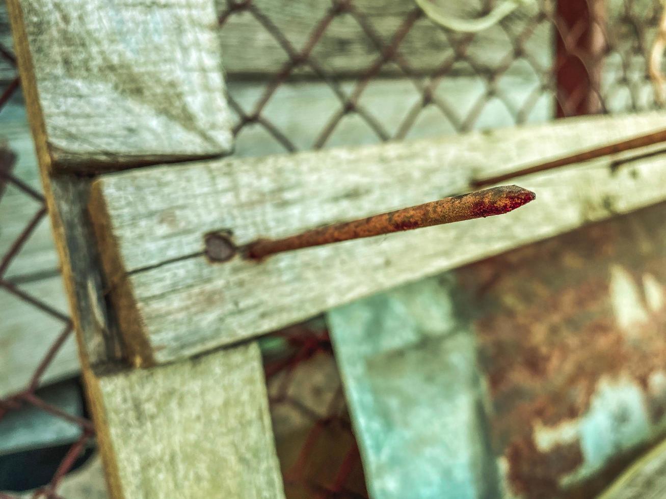 A large long rusty old iron metal construction industrial nail sticks out of a wooden plank photo