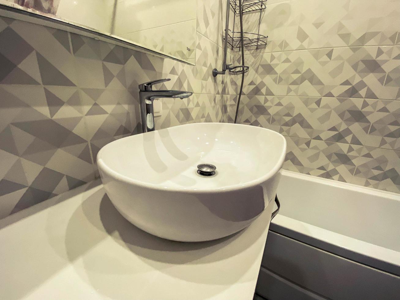 modern, stylish bath in a residential apartment. a huge sink made of white material, a stone countertop mounted on cabinets with shelves. stylish geometry on the tile photo