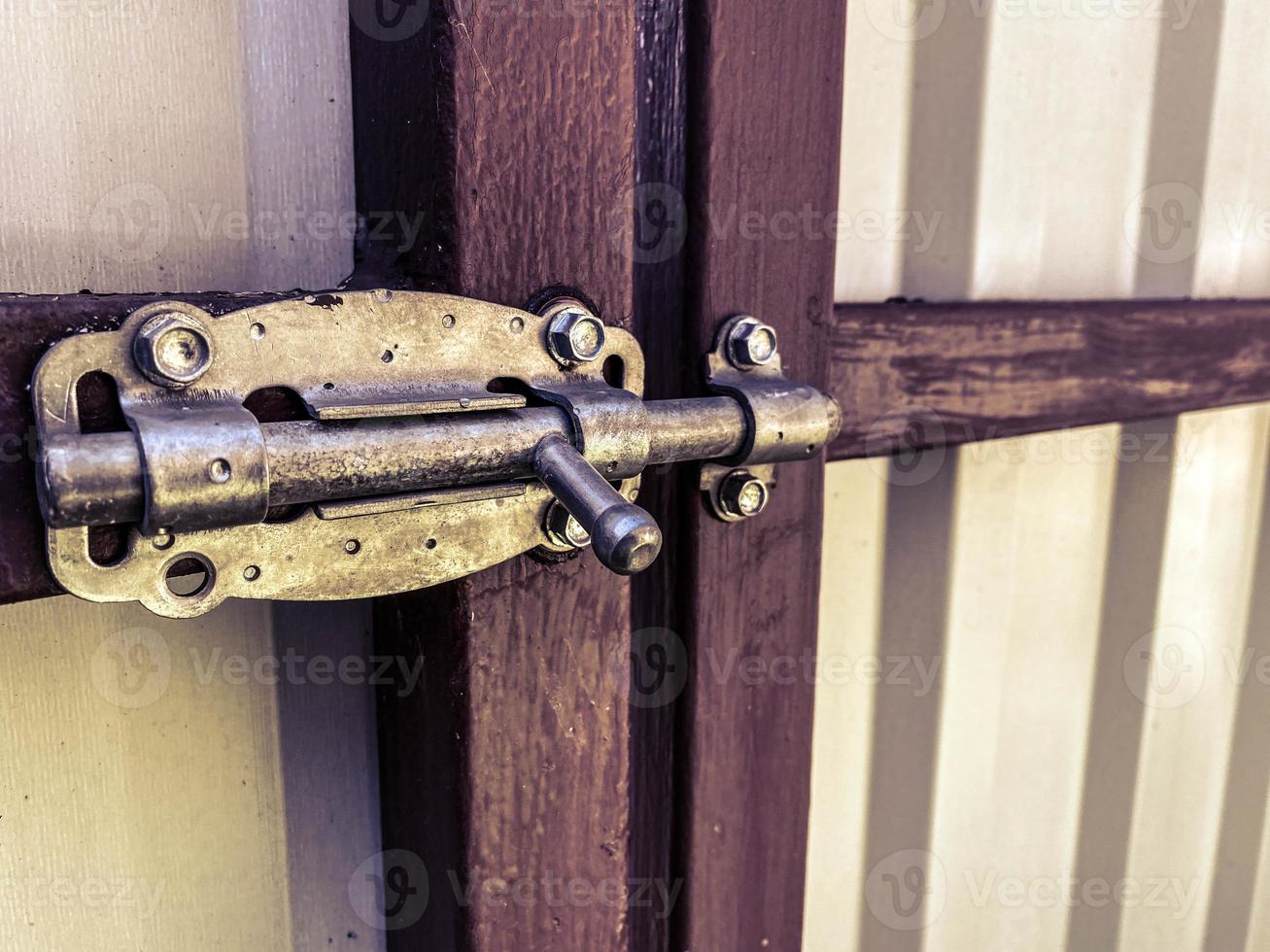 A metal wire fence door of junk room is closed with row of general type garbage bins as blurred background. Close-up and selective focus at the door's latch object part photo