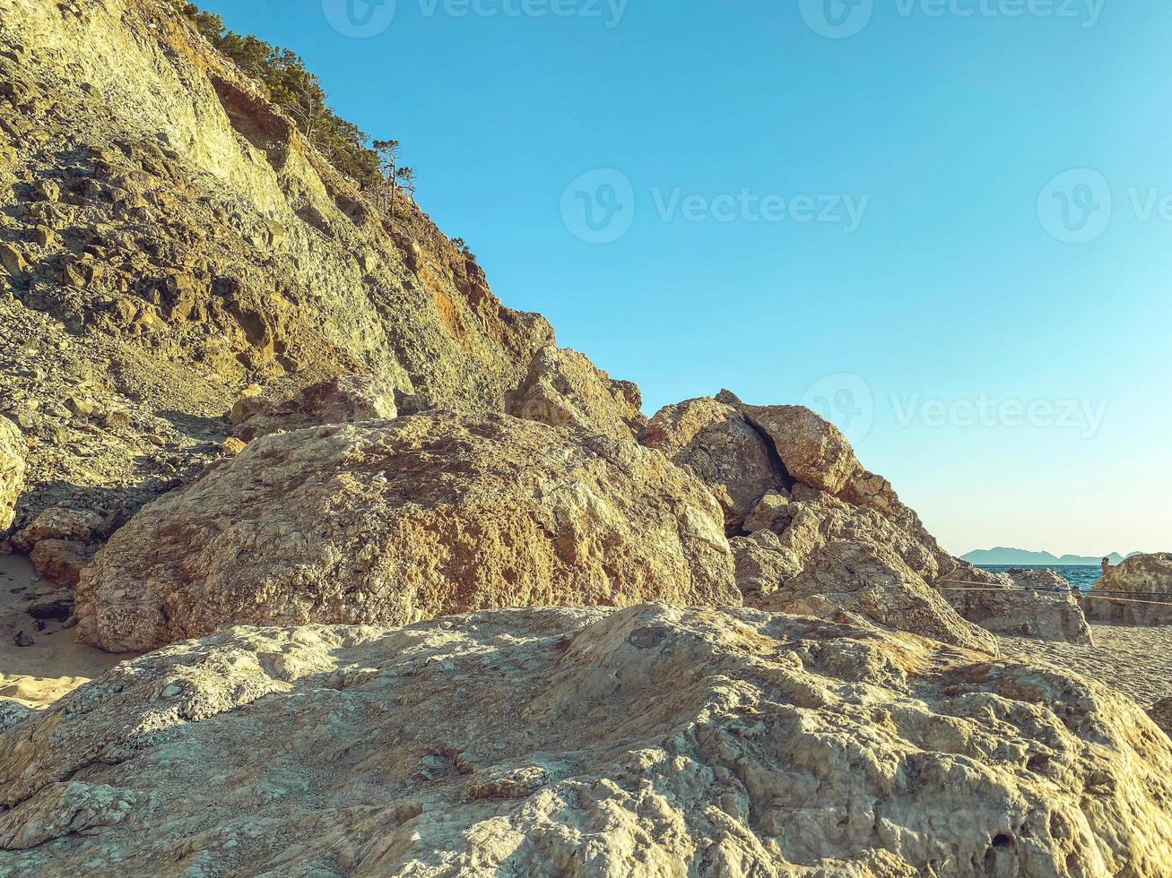 huge stones lie on the beach near the sea. huge boulder of sand, rock. a stone lies on the seashore and is washed by water against the background of a blue sky photo