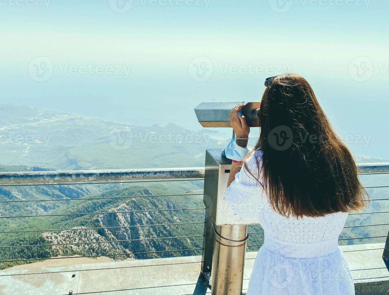 a girl in a white dress with long hair looks through binoculars on an observation platform. observing the view from the mountains from a great height in an early country photo