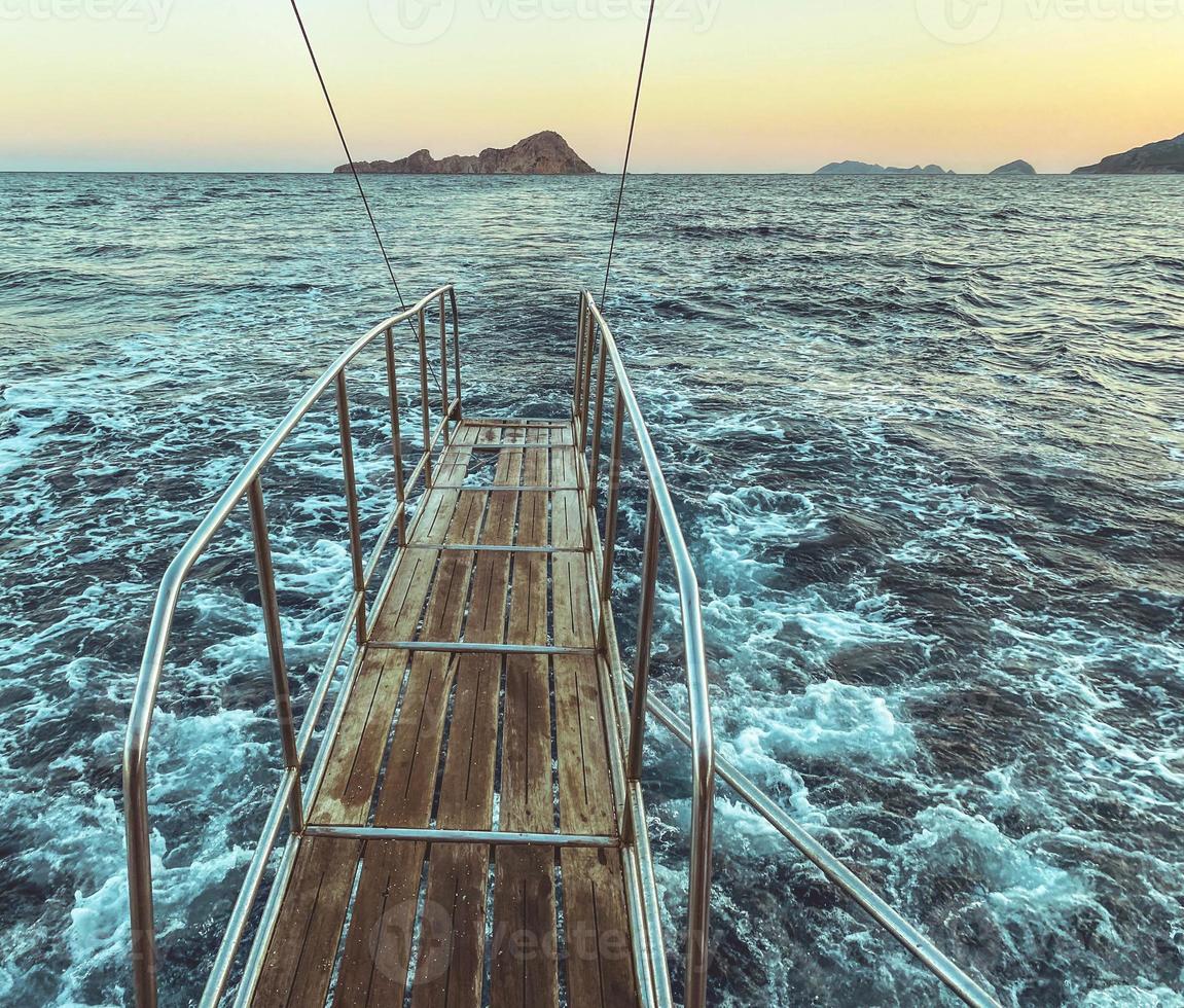 bridge made of wood with metal breaks into the sea. water with white foam, blue waves. bridge on a yacht for bathing tourists, jumping into the water from a height photo