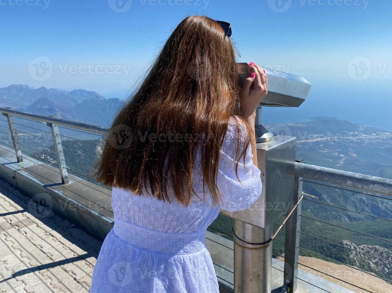 Back view of active senior woman with backpack on vacation looking through binoculars at mountains. Focus on mountains photo