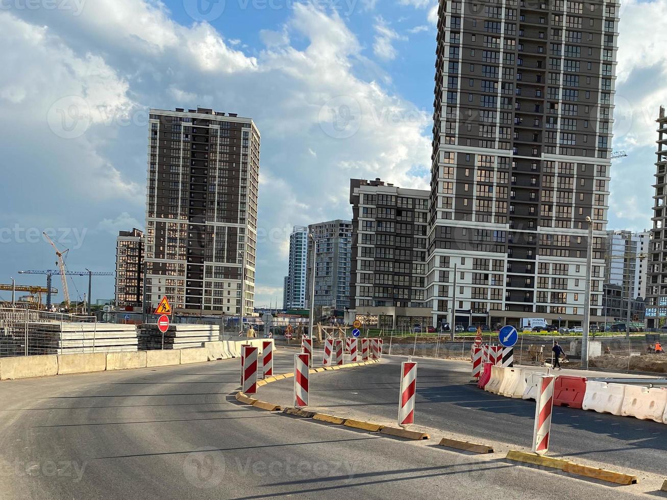 Repair and construction of a road with temporary road signs and cones against the background of beautiful tall new buildings against the background of blue sky and rainbow in a big city photo