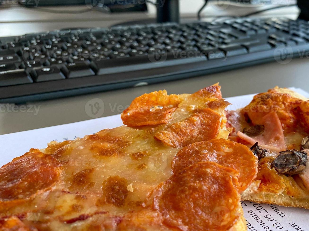 Desktop mix with office gadgets, supplies and pizza on a wooden office table background. View from above photo