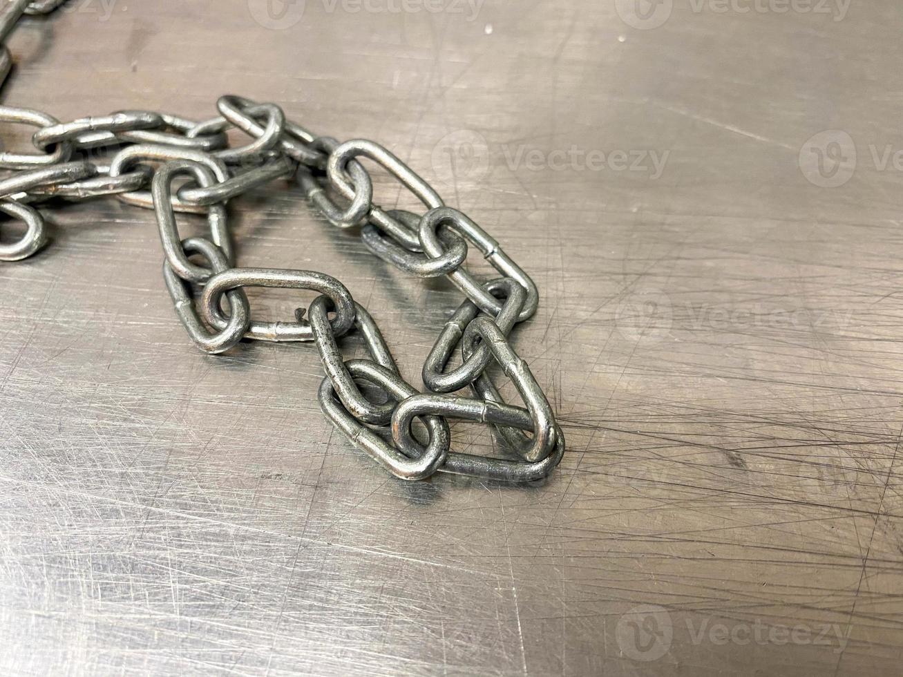 A large iron metal strong powerful shiny chain with links lies on an iron industrial table. Hand-held locksmith tools. The background photo