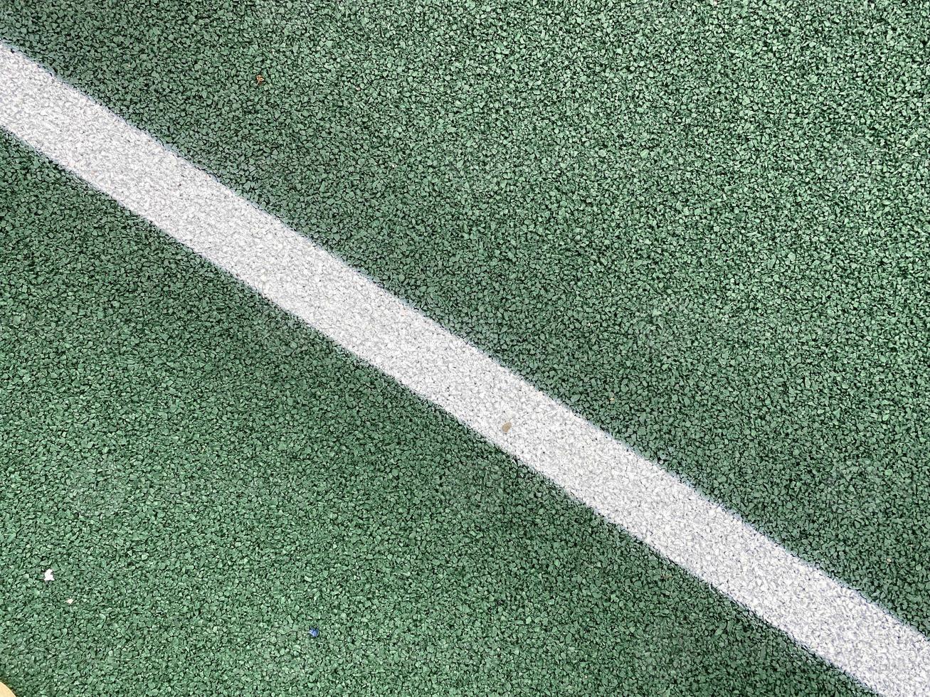 Green rubber surface of a tennis court anti-traumatic safety tile on a workout sports playground in a public park or courtyard. The background. Texture photo