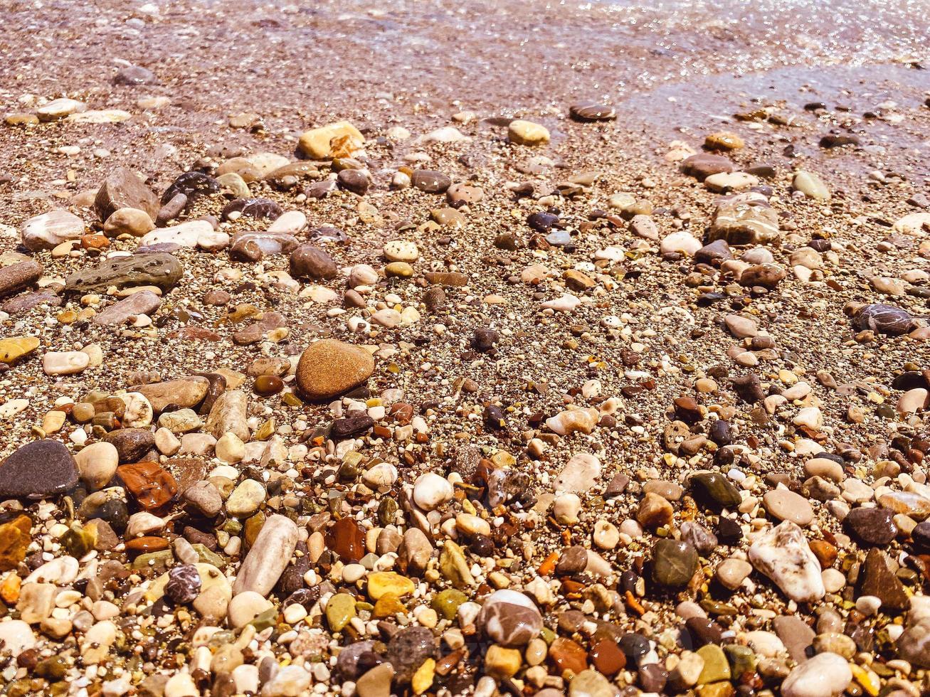 vacation by the sea on the beach. pebble beach with stones. wet, small, multi-colored stones near the water, waves with white foam wash the stones on the shore photo