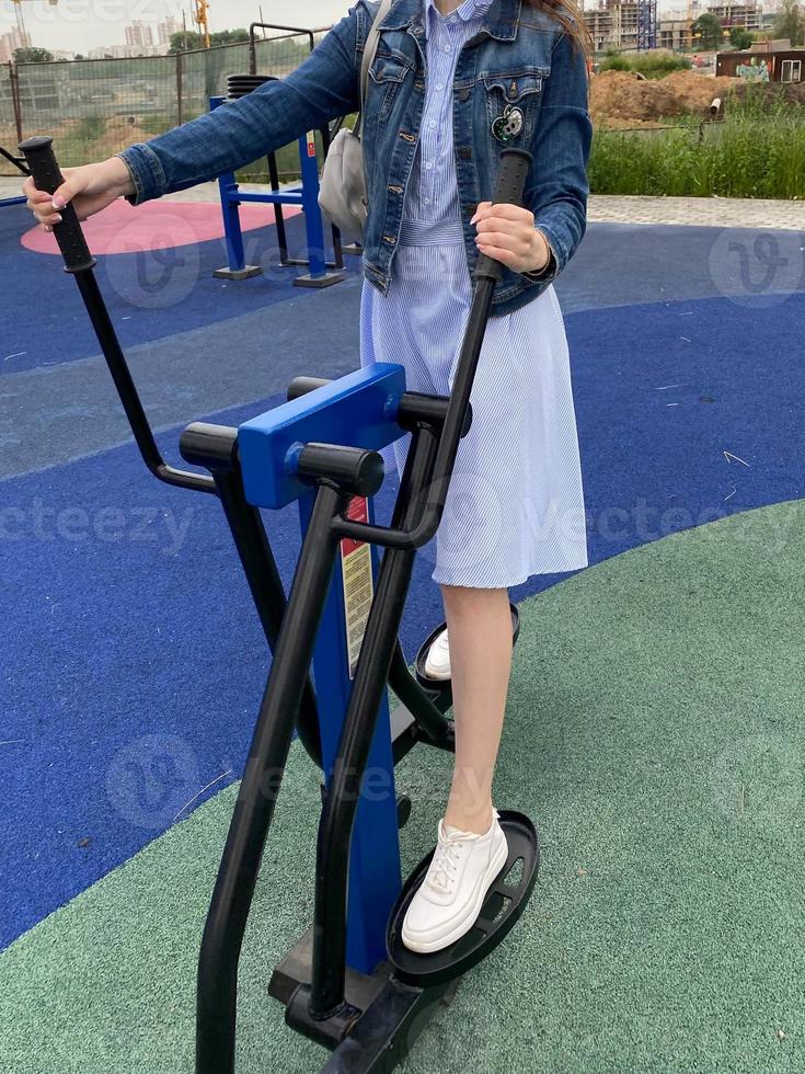 A woman goes in for sports on a new modern blue fitness leg trainer for walking and running on an outdoor workout site photo