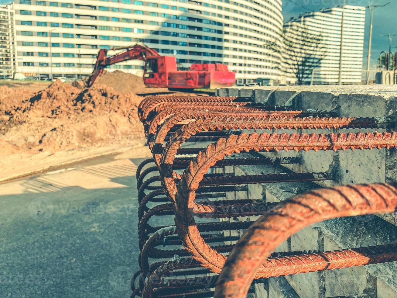 concrete block with rusty rebar sticking out inside. fixtures for building houses. blocks on the background of a red excavator photo