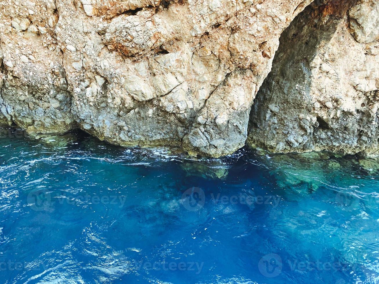 the blue sea beats waves against the rock. mountain on the coast. holidays in warm countries. the texture of the mountain, the rock with a 3D volume photo