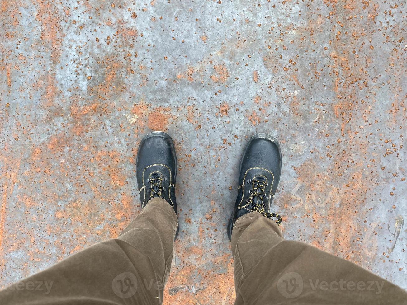 Legs of a man in boots on the background of a rusty old iron red scratched metal corrosed sheet surface background, texture industrial in loft style photo