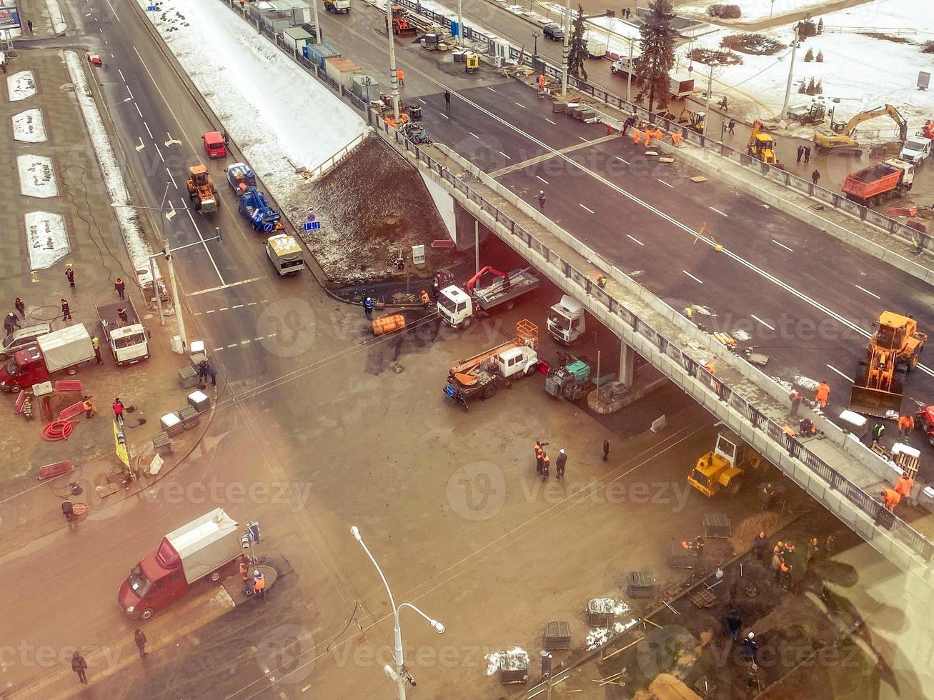 construcción de un nuevo puente en el centro de la ciudad, vista desde arriba. maquinaria de construcción está trabajando en la colocación de nuevo asfalto. congestión de coches debajo del puente foto