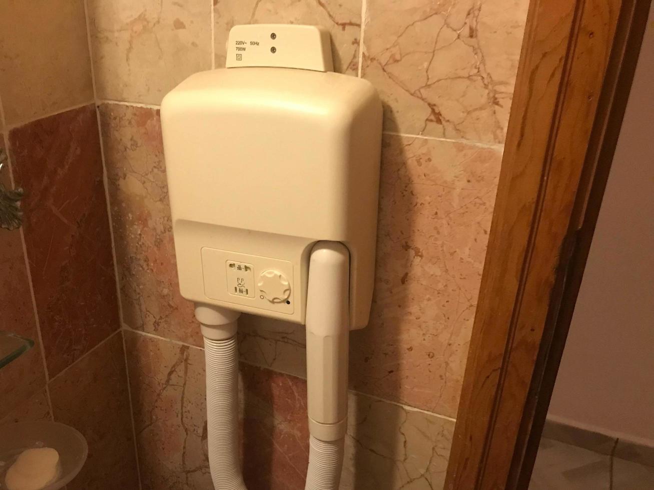 old bad stationary white plastic hair dryer in hotel on bathroom wall photo