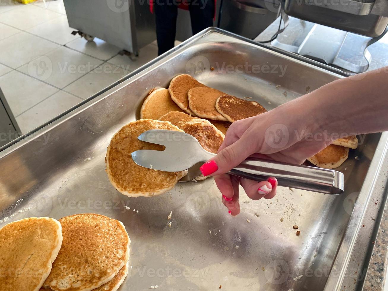 A beautiful hand of a girl takes with tongs delicious flour pancakes for breakfast from a plate in a canteen cafe. The background. Texture photo