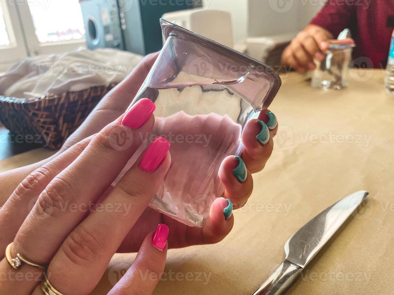 chica con anillos de oro en los dedos y manicura brillante. uñas azules y rosas. en manos de una niña un vaso transparente con agua limpia y potable foto