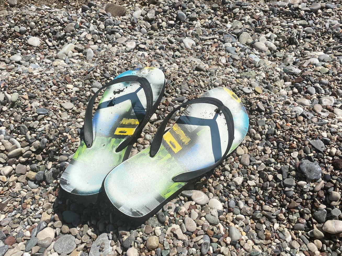 Beach scene with flip flop sandals lying on sea coquina shells and pebbles on the beach. Travel concept photo