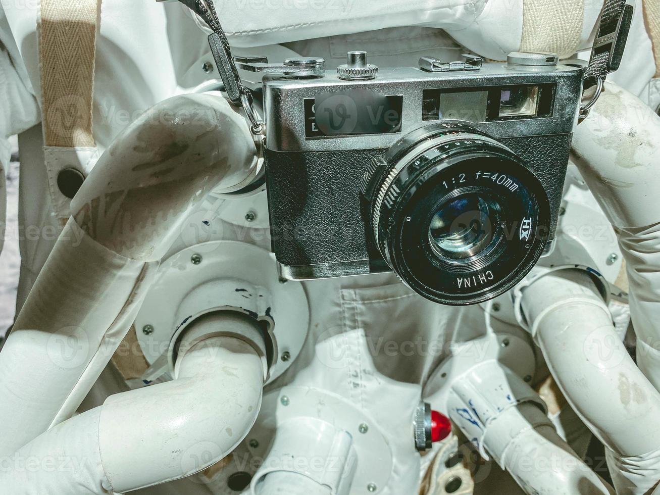 traje blanco con traje espacial astronauta en el espacio. tiene una pequeña cámara vintage colgada de su cuello. filmando en la atmosfera foto