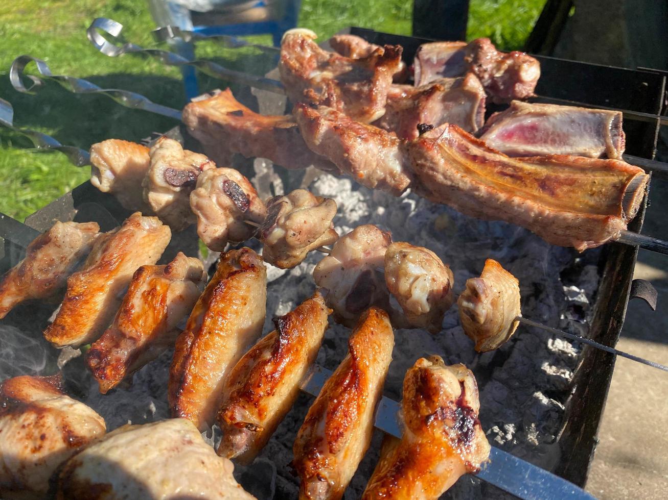 Delicious beautiful fried kebab of pork meat, chicken wings and pork ribs on the smoke cooked on the grill with skewers with coals. Barbecue in nature. BBQ photo