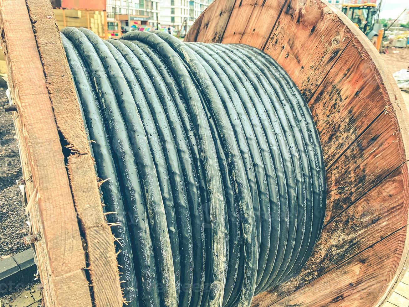 reel made of wood at a construction site. a black, long cable is wound on the coil to create communications. wires for laying in a new microdistrict photo