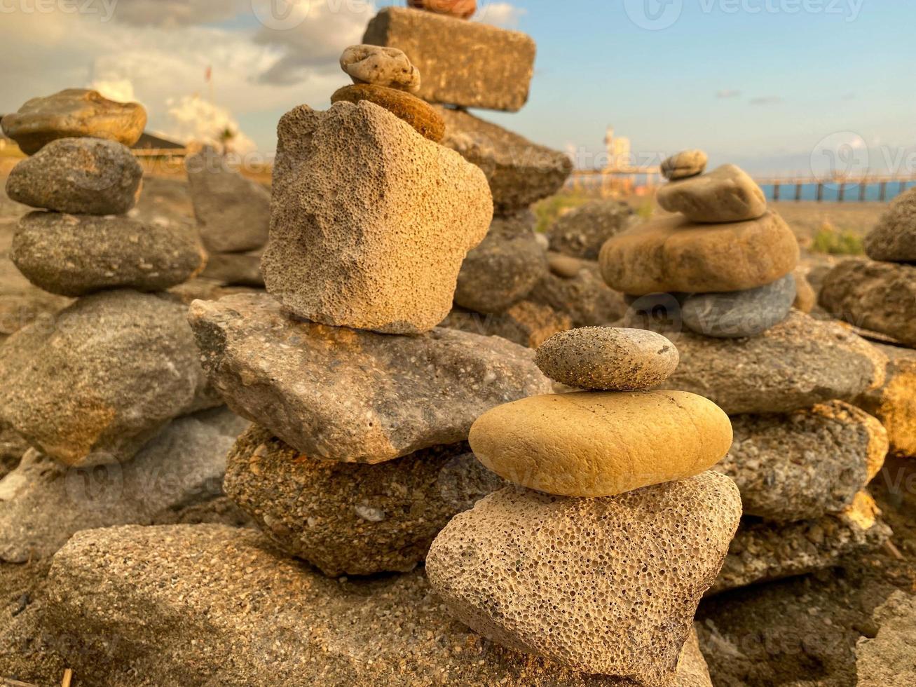 A pyramid of stones stacked on top of each other on the beach and sand with small natural multi-colored stones on the shore against the backdrop of the sea at sunset photo