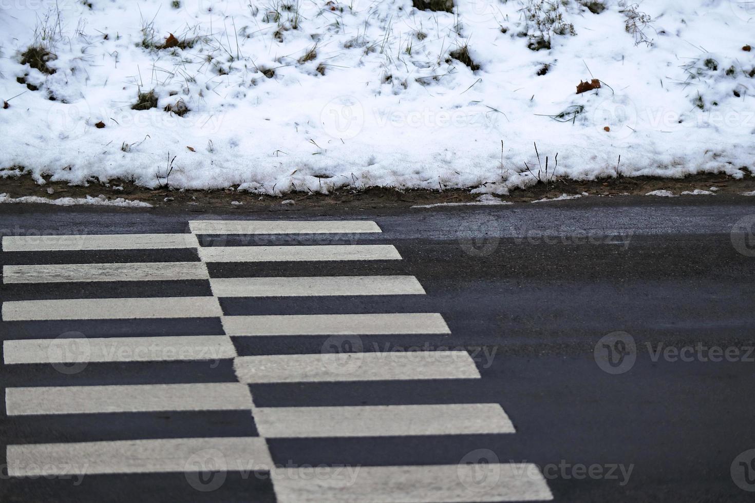 Road crossing zebra on black wet asphalt road with snow covered sides low angle view photo