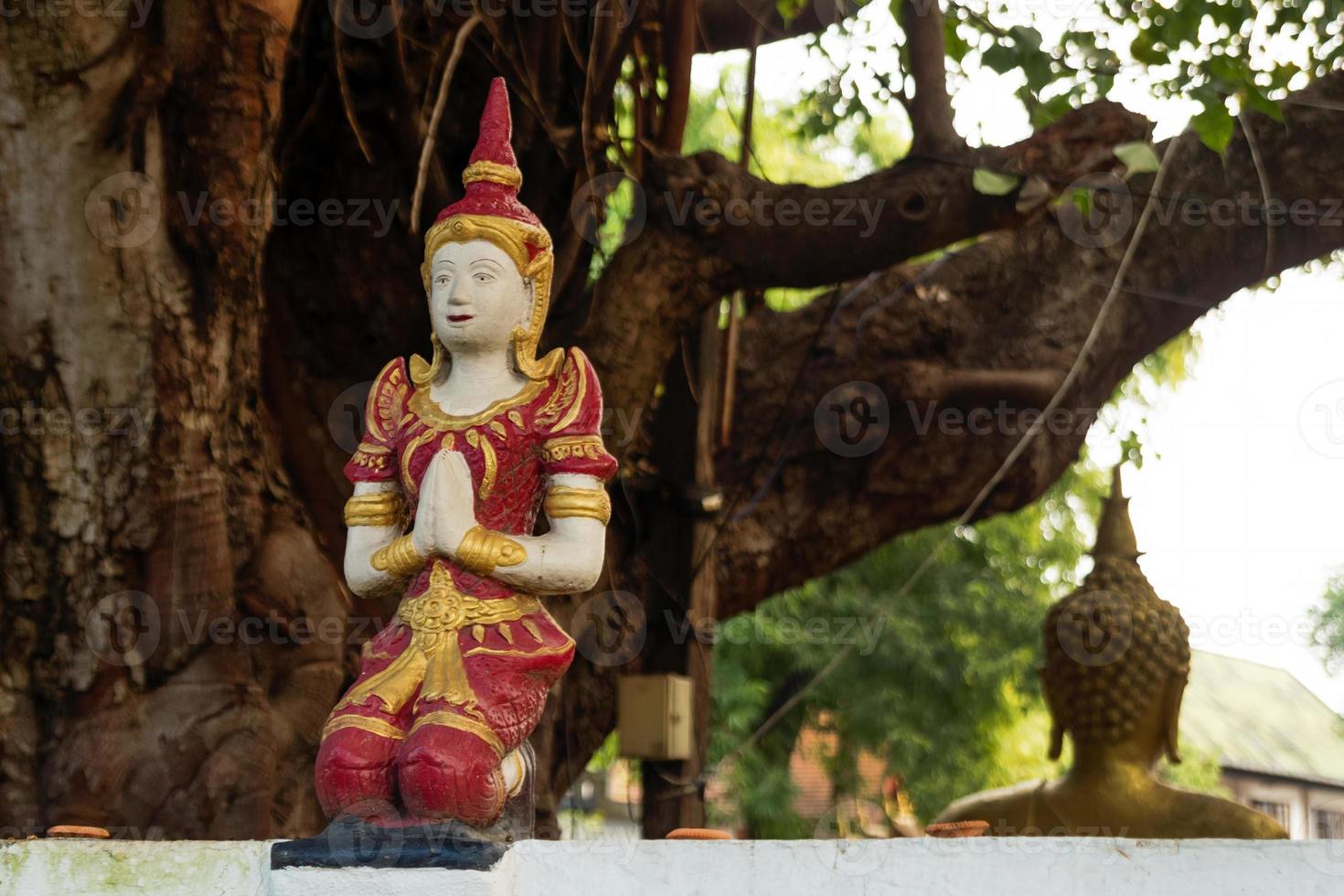 Small stone red and gold statue Buddha near to temple on a background of tree. Chiang Mai, Thailand. photo