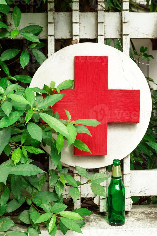 cruz médica de madera roja y blanca y botella de cerveza vacía cerca de la clínica. foto