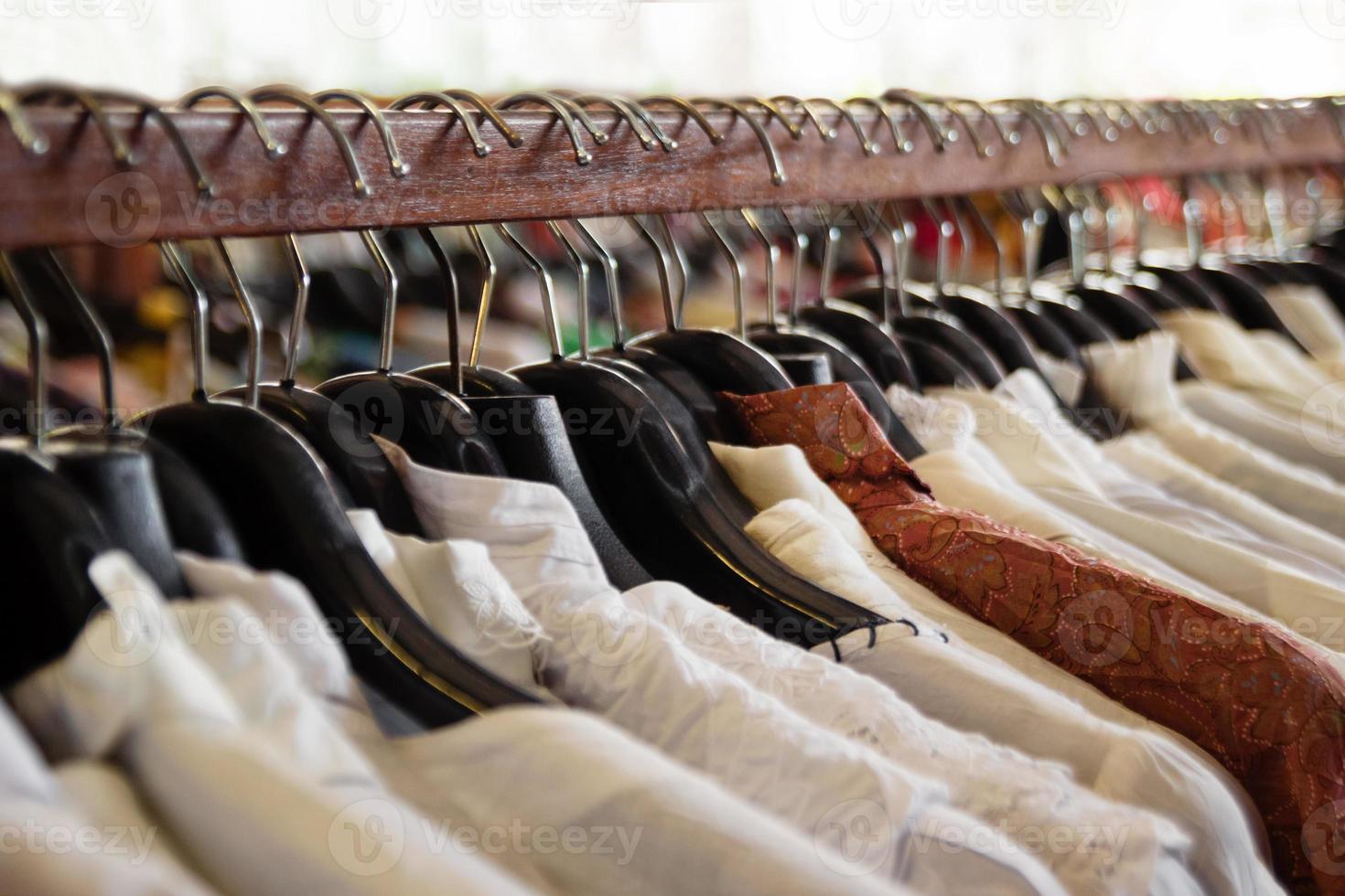 percheros de madera con perchas y camisas blancas y marrones dentro de una tienda. foto